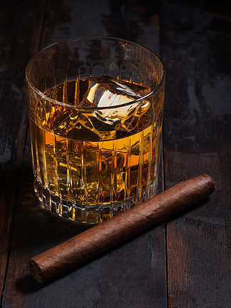 水晶玻璃杯中的单一麦芽苏格兰威士忌，木桌背景上有冰块和古巴雪茄。