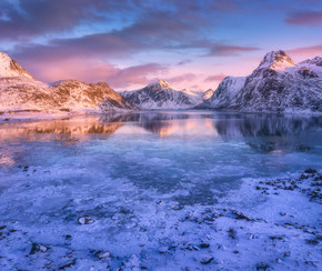 雪山的鸟瞰图，蓝色的大海与寒冷的海岸，水中的倒影，色彩缤纷的日落时天空与粉红色的云彩。挪威罗弗敦群岛。与积雪的岩石、峡湾、冰的冬天风景