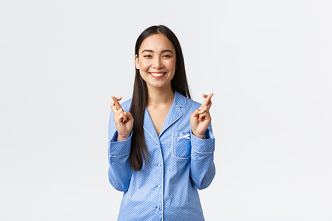 穿著藍色睡衣的快樂微笑亞洲女孩相信夢想成真,交叉手指好運氣,許願