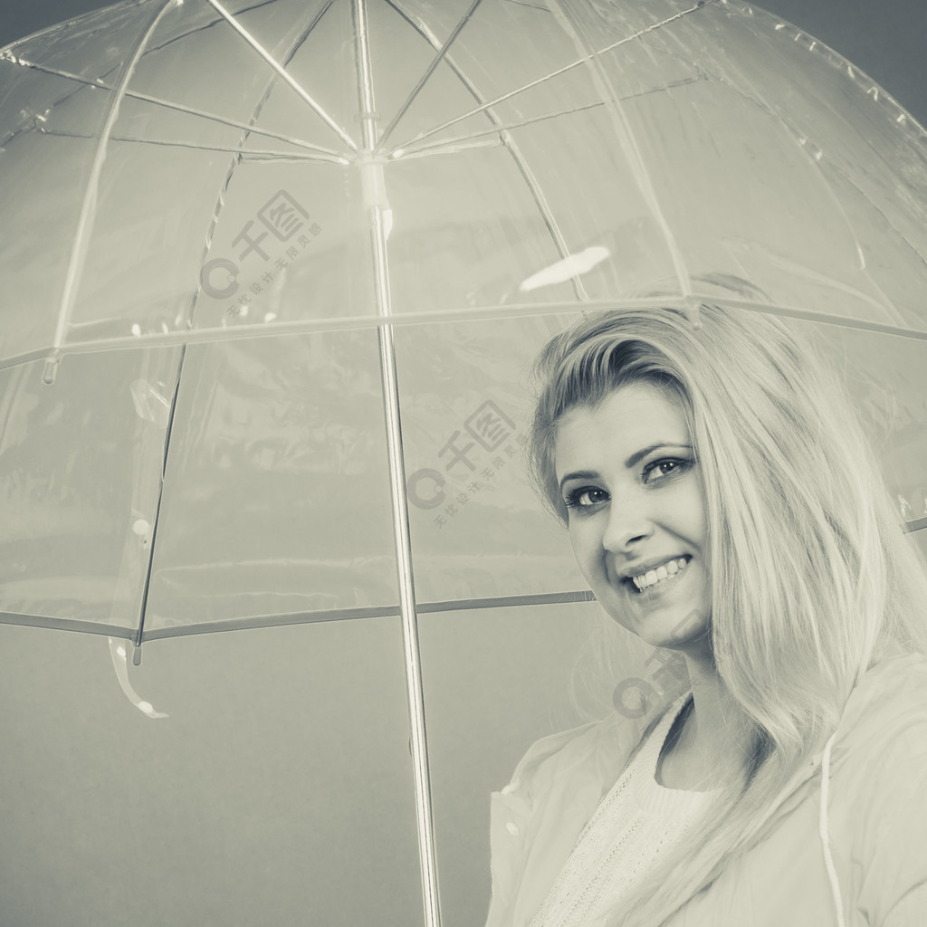 下雨天心情好快乐的金发女人穿着雨衣拿着透明的雨伞