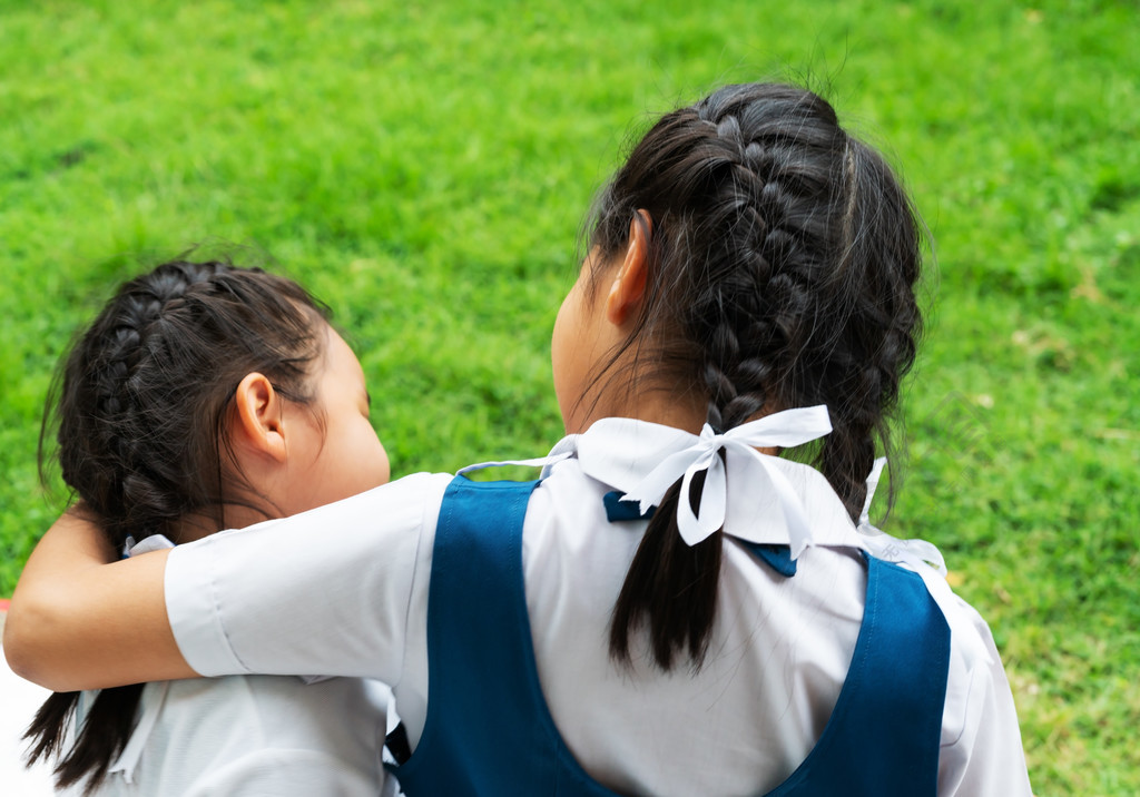 两个亚洲小女孩姐妹穿着校服拥抱快乐的岗位回到学校的概念