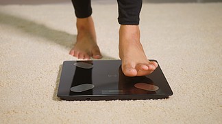 亚洲年轻女性腿踩在地板电子秤上，女性在家客厅锻炼，女性站在数字称重机上。健康减重控制概念，慢动作
