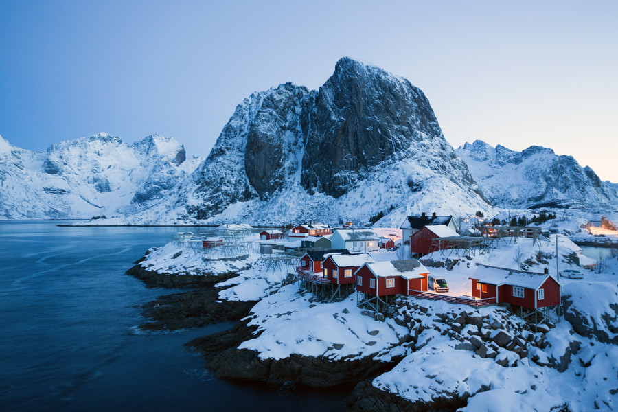传统的挪威红木屋 rorbu 矗立在峡湾的岸边,远处的群山罗弗敦群岛