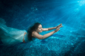 穿着裙子的漂亮女人的水下照片在光束下从游泳池里冒出来