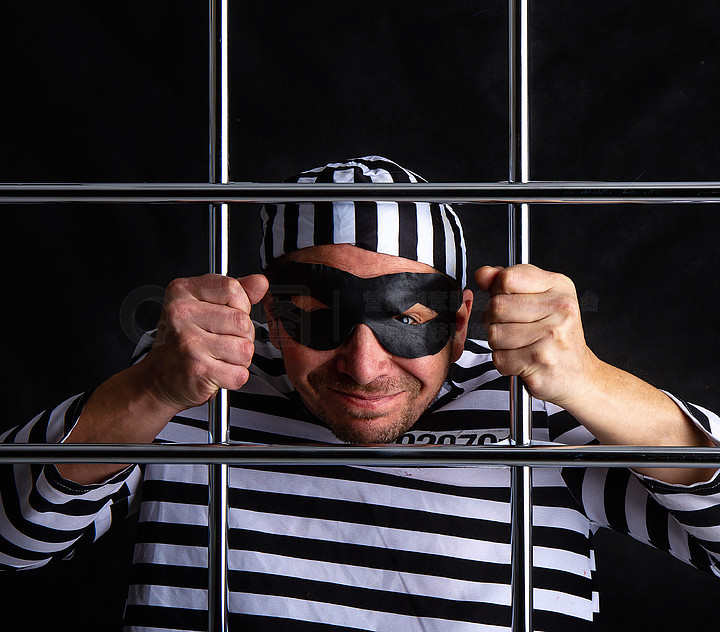 一个身着条纹囚犯服装和黑色面具的漫画暴徒坐在金属栏后面的监狱里