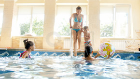 快乐开朗的家庭在游泳池玩乐的形象。年轻的母亲带着三个孩子在带游泳池的健身房里。快乐开朗的家庭在游泳池玩乐的照片。带三个孩子的年轻母亲在带游泳池的健身房里