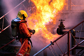 消防员使用水雾式灭火器与石油钻井平台和天然气站石油管道泄漏和<i>爆</i><i>炸</i>产生的火焰作斗争。消防员和工业安全概念。
