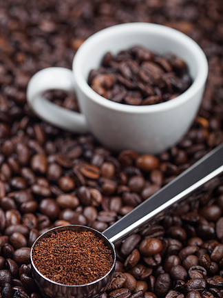 新鲜的生有机磨碎的咖啡粉，黑色钢勺，咖啡豆顶部有白色浓缩咖啡杯。宏