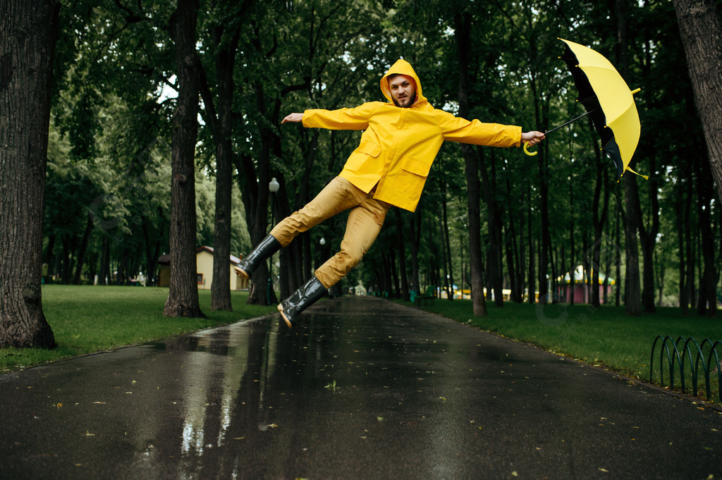 男子在大风雨天在夏日公园里撑着伞飞翔穿着雨披和橡
