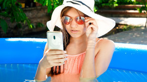 美丽的 teengae 女孩躺在游泳池里，在智能手机上浏览互联网或社交媒体。愉快的暑假和假期的概念。美丽的少女躺在游泳池里，在智能手机上浏览互联网或社交媒体。愉快的暑假和假期的概念