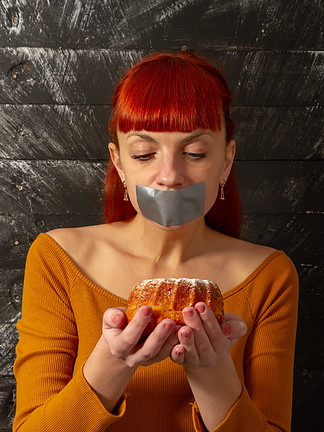 一个年轻的红发女孩节食的概念形象，她的嘴在开胃糕点前用银胶带<i>粘</i>住。减肥唇膏