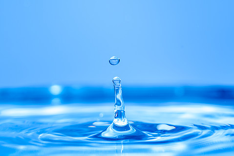水滴溅入水晶般清澈的蓝色水中,形成涟漪背景一滴清水