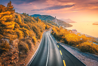 秋季色彩缤纷的日落时分，鸟瞰山路和美丽的橙色森林。克罗地亚杜布罗夫尼克。秋天的道路、树木、大海、山脉、红色天空的顶视图。景观与高速公路和海岸