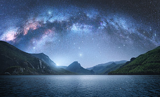夏季夜晚，<i>拱</i>形银河在美丽的山脉和蔚蓝的大海上空。五颜六色的风景与明亮的星空与银河<i>拱</i><i>门</i>、月光、星座、水。星系。自然与空间。夜间<i>拱</i>形银河在群山和蔚蓝的大海上