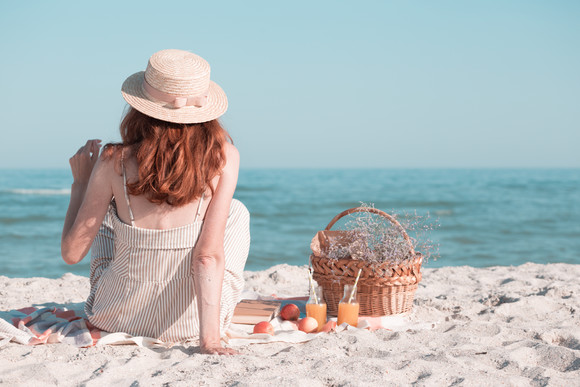 夏天-海边野餐。戴着帽子和篮子的女孩带着面包、苹果和果汁去野餐。