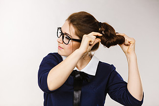 戴眼镜的女商人、会计师或老师固定她的发型。灰色背景。修理她的头发的女商人