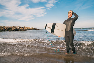 年轻的冲<i>浪</i>者穿着黑色冲<i>浪</i>服站在海里，他的冲<i>浪</i>板。运动和水上运动的概念。