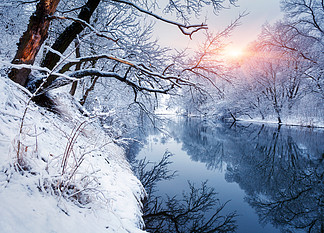 日落时河上的冬季森林。五颜六色的风景与白雪皑皑的树木，河流在<i>寒</i>冷的夜晚在水中倒影。白雪覆盖的树木、湖泊、阳光和蓝天。下雪的冬天美丽的森林。日落时河上的冬季森林。五颜六色的风景与白雪皑皑的树木<i>冷</i><i>冷</i>