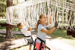 勇敢的小孩子在绳索公园、操场上爬网。孩子们在吊桥上攀爬，假期极限运动冒险，户外危险娱乐。勇敢的小孩子在绳索公园爬上网