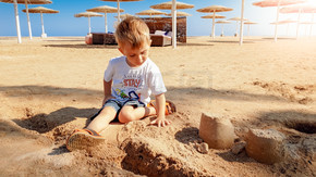 3 岁蹒跚学步的小男孩坐在沙滩上用湿沙建造城堡的照片。 3 岁小男孩坐在沙滩上用湿沙建造城堡的形象