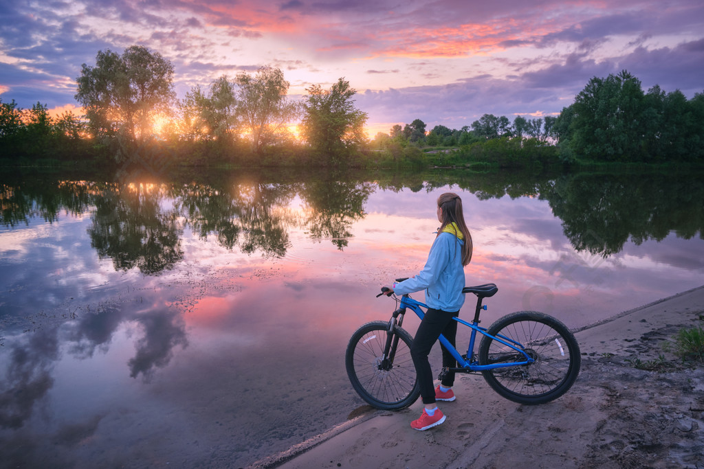 夏天日落时在河岸上骑自行车的女人风景与年轻女孩与山地自行车沙滩