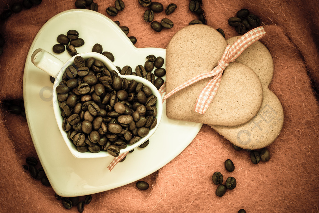 咖啡爱情观咖啡豆在心形的白色杯子和甜饼干姜饼与棕色布背景上的丝带
