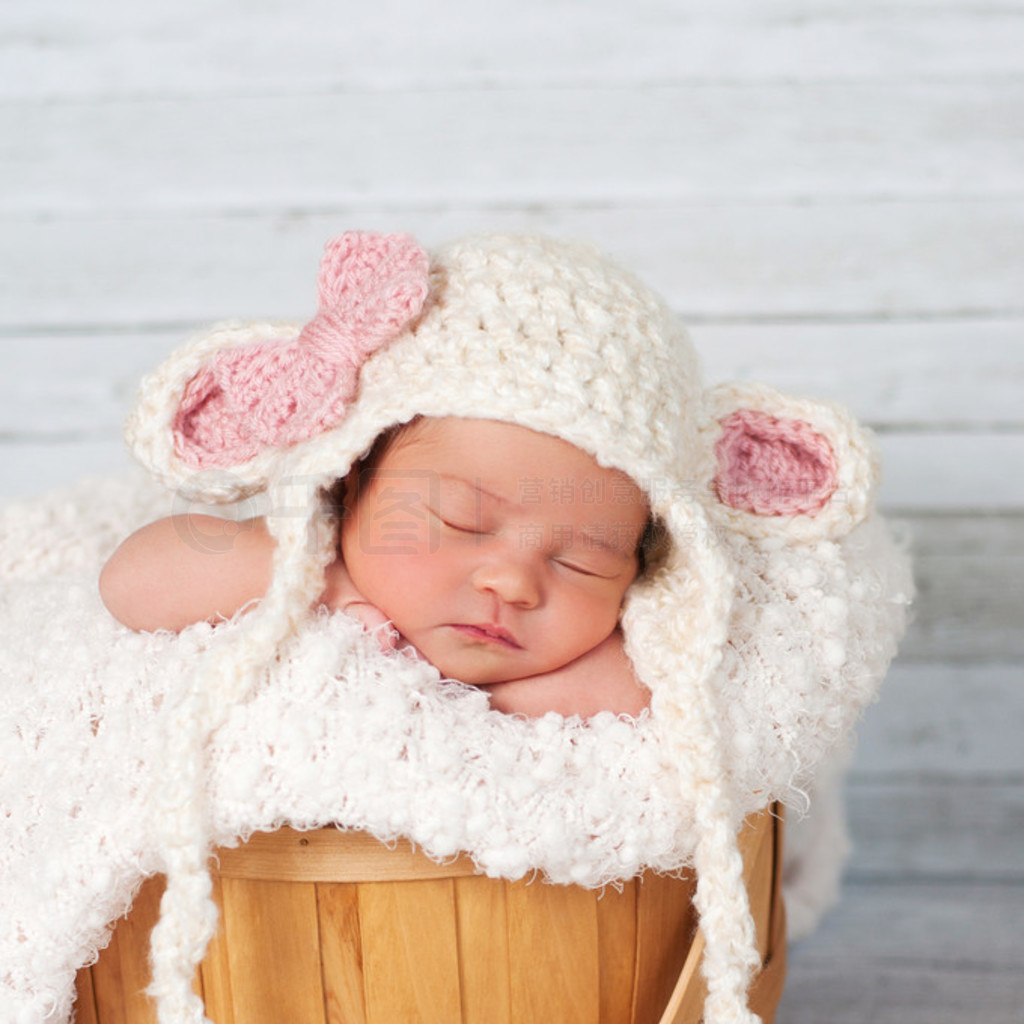 Newborn girl wearing a crocheted lamb hat and sitting in a basket