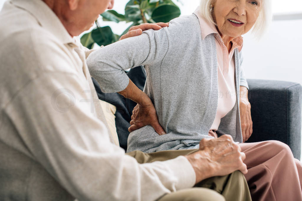 cropped view of husband looking at wife with back pain in apartment