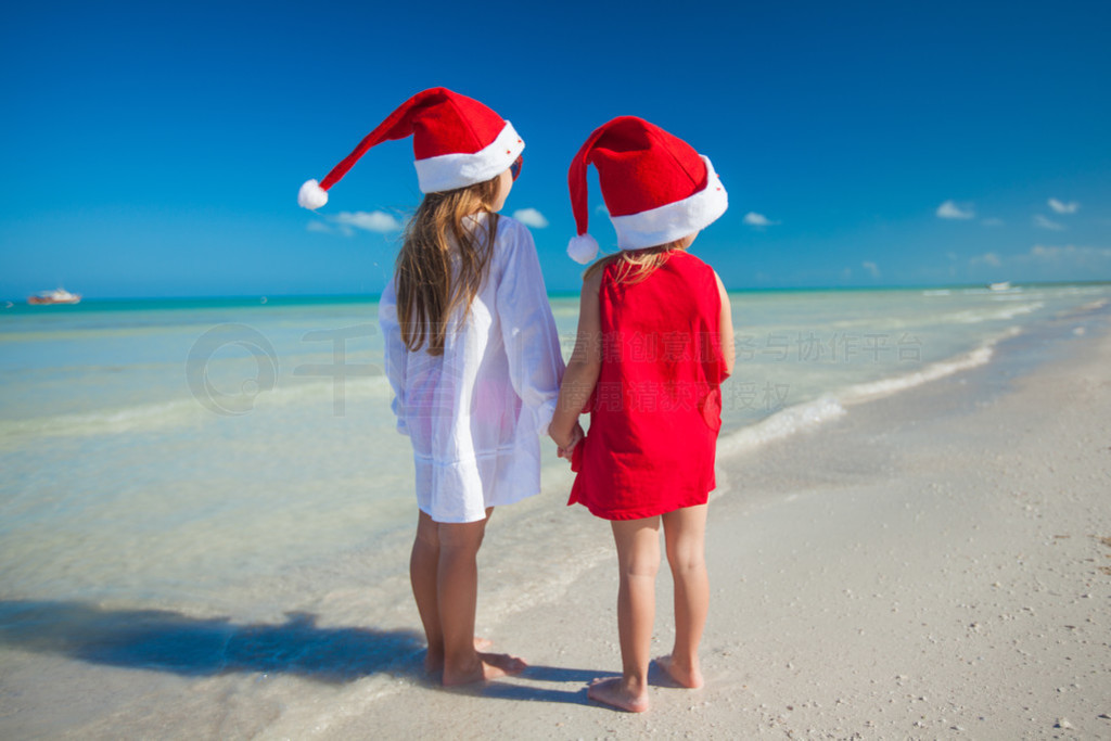 Back view of Little cute girls?in Christmas hats on the exotic beach