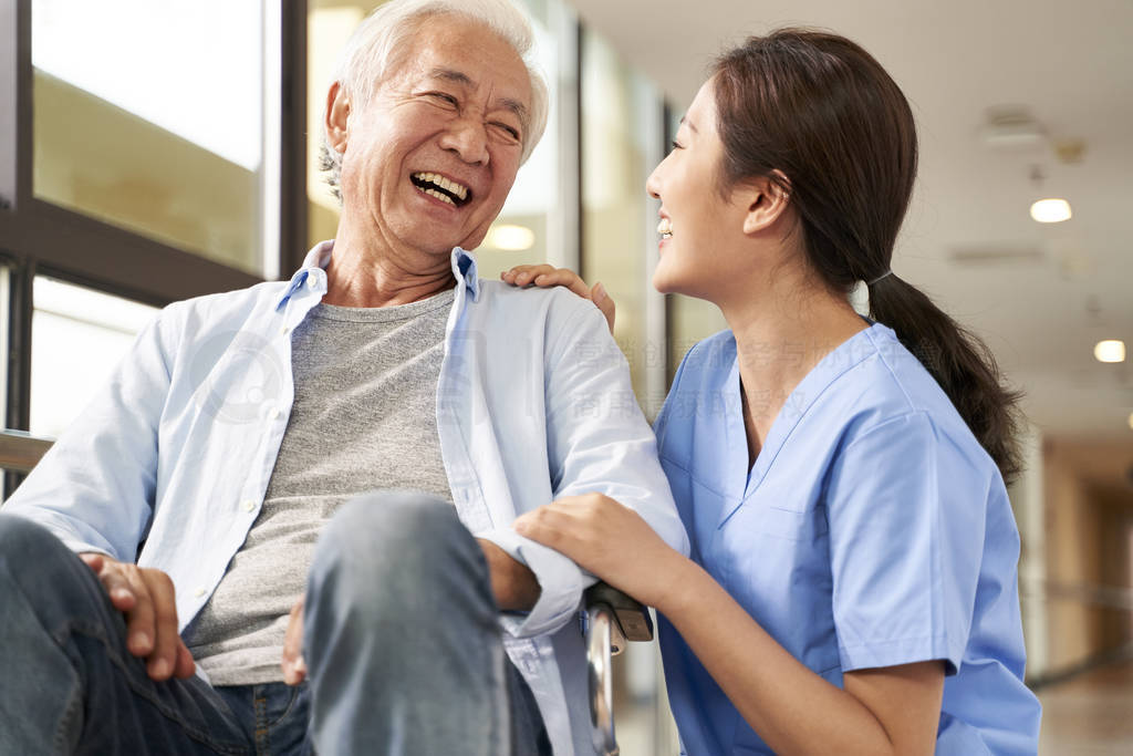 young friendly asian female caregiver talking to elderly man in