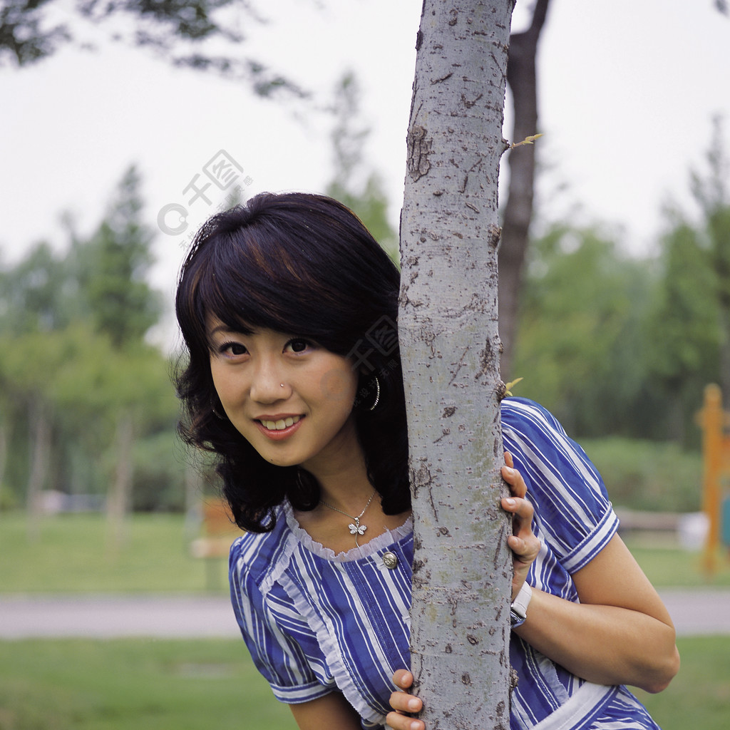 亚洲站韩国在户外女人季节春天白天阳光照片蓝色树背景公园笑特写镜吞