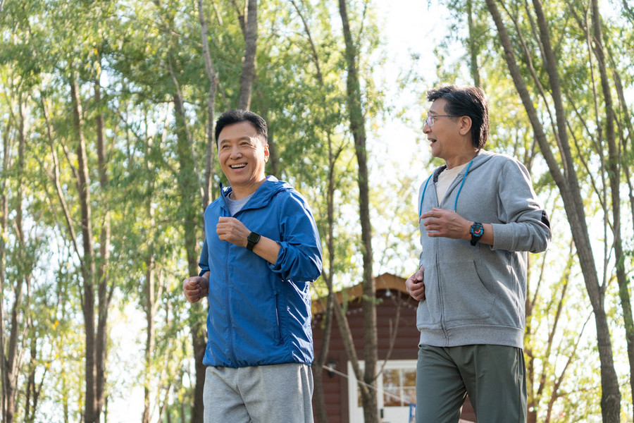 兩戴運動手錶的中老年男人在樹林裡跑步健身