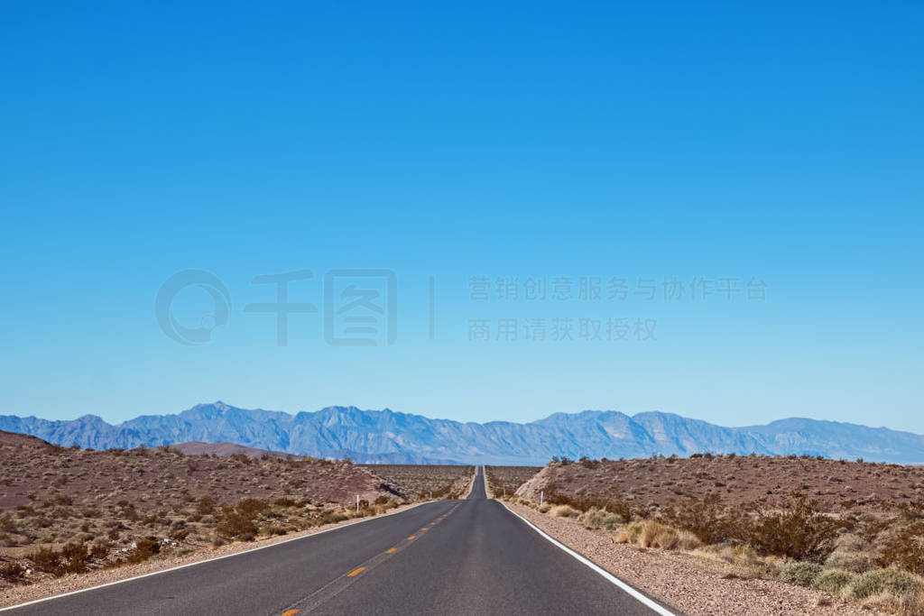 Empty asphalt road through the desert in a sunny day with mounta