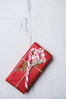 漂亮的红色圣诞礼品盒，上面有棍子和杉树枝，躺在白色的木头表面上。平躺在头顶上。把注意力集中在礼物包装上