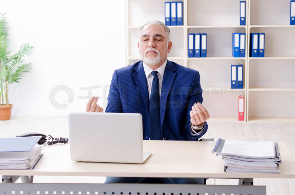 Aged businessman doing yoga exercises in the office