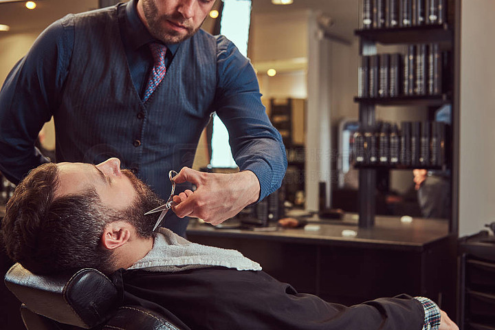 专业理发师建模胡子与剪刀和梳子在理发店特写照片