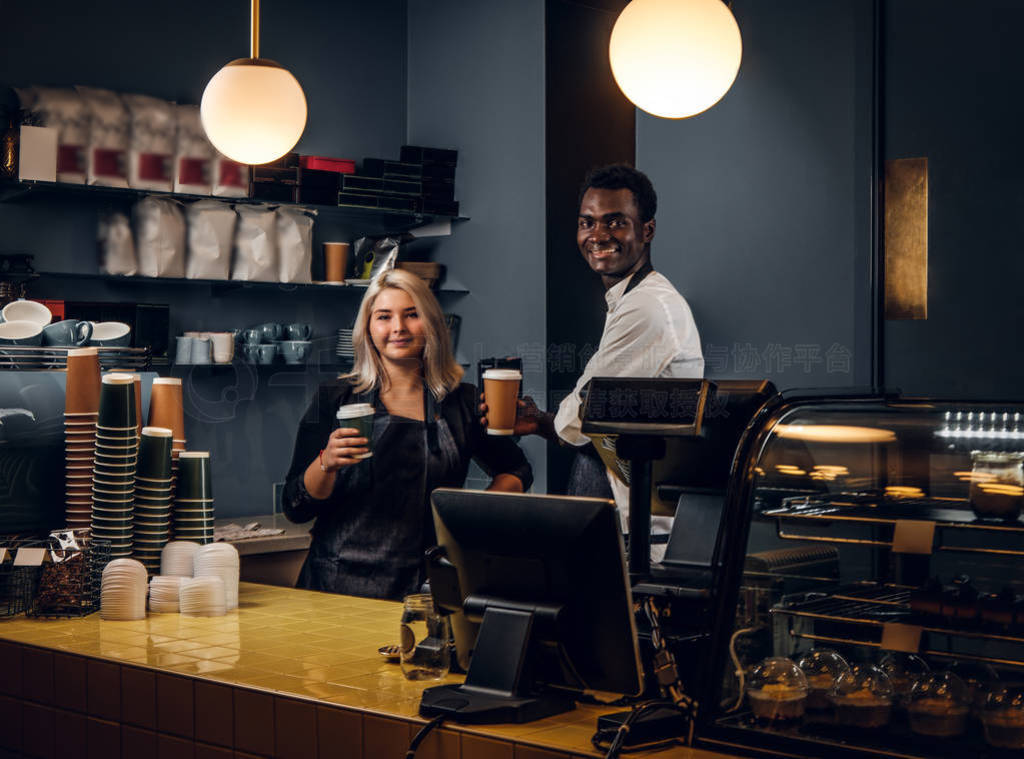 Two multiracial baristas holding a coffee while standing behind
