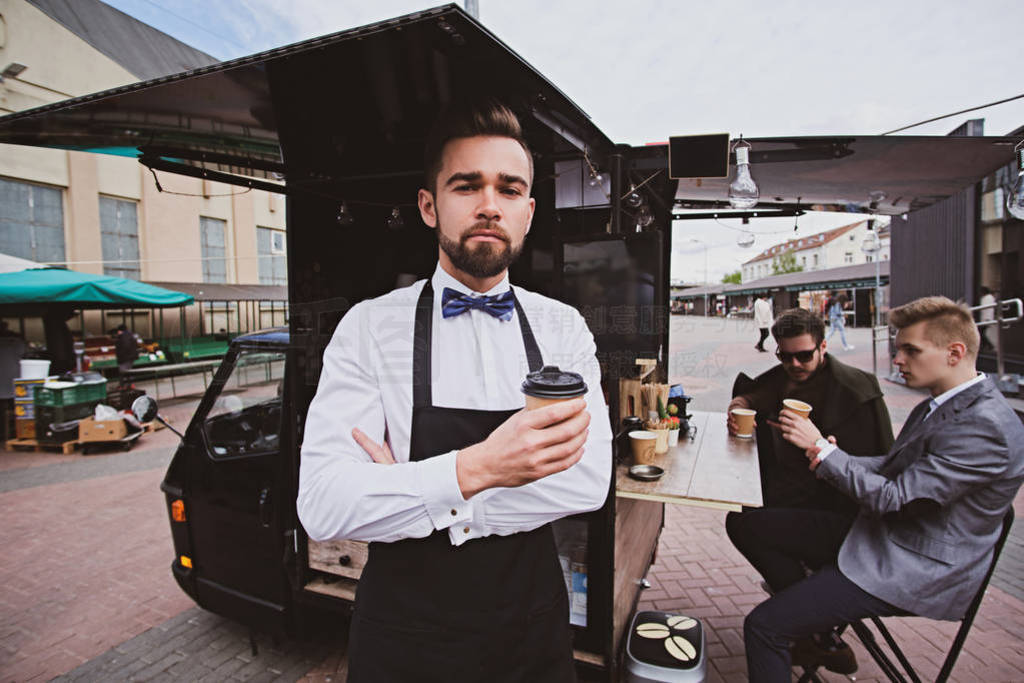 Elegant barista is standing crossed his hands next to his coffee