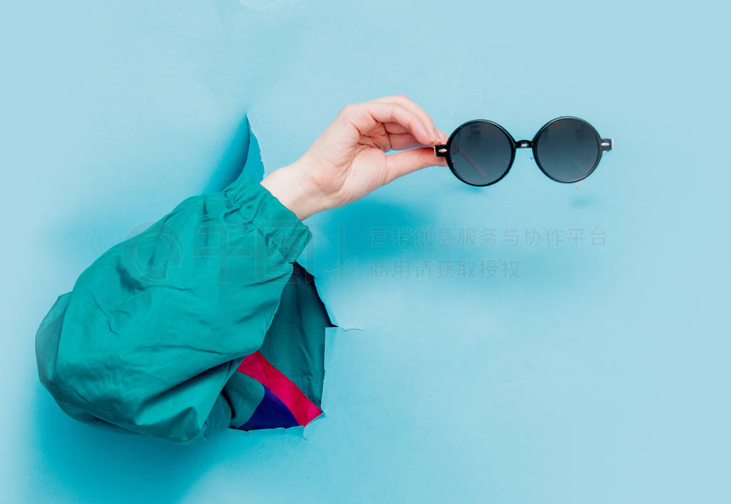 Female hand in 90s style jacket holding suglasses