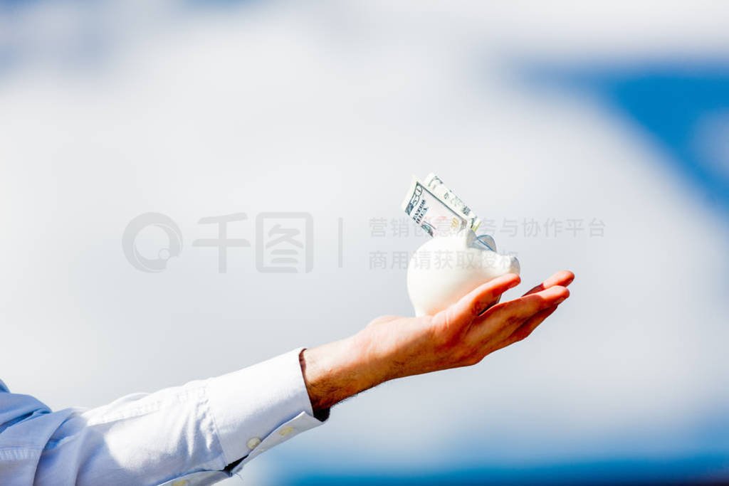 Male hand holding piggy bank with cash dollars