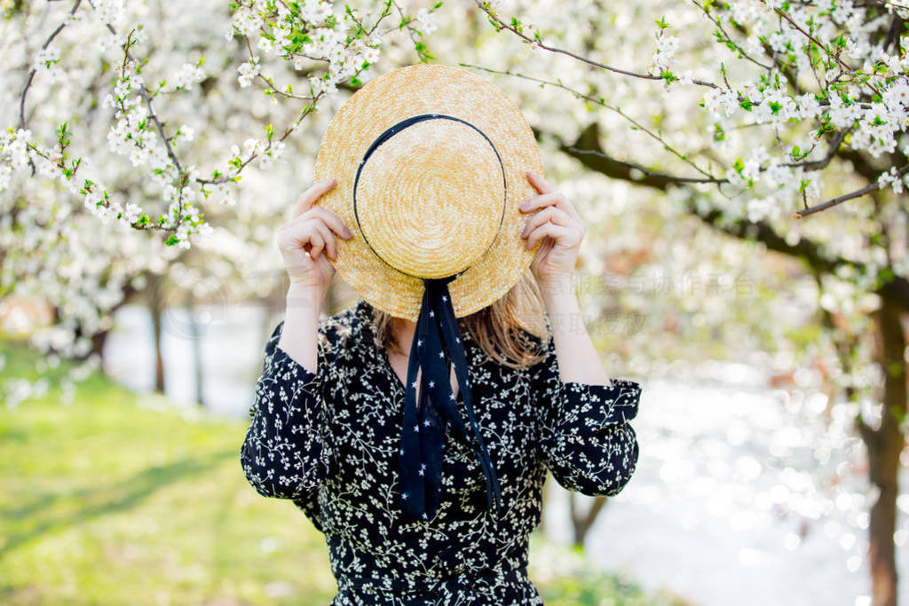 Young girl in a hat stay near a flowering tree