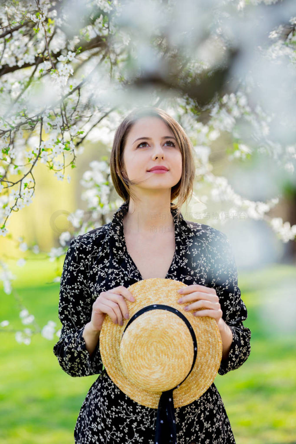 Young girl in a hat stay near a flowering tree