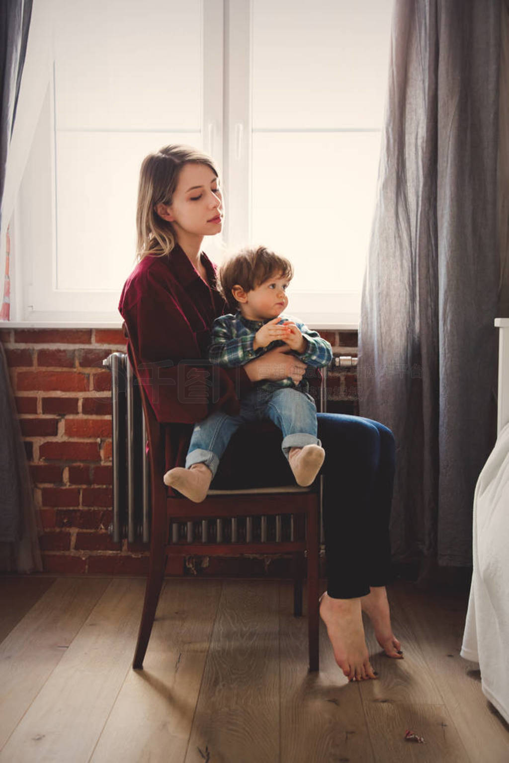 Mother and toddler boy sitting on chair near window