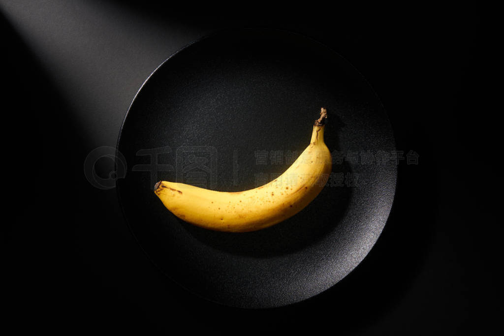 Banana in black plate on black background with ray of light