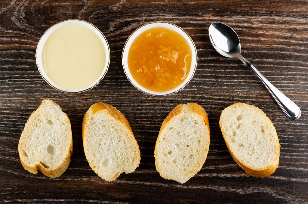Bowls with condensed milk, lemon jam, spoon, slices of bread on