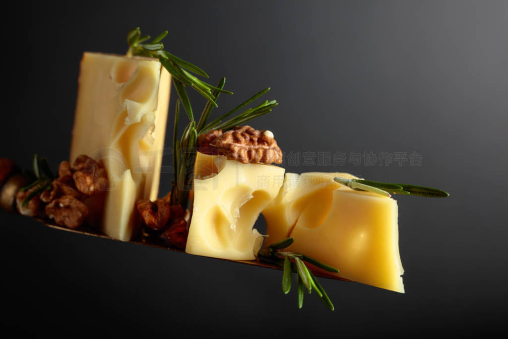 Maasdam cheese with walnuts and rosemary on a black background.