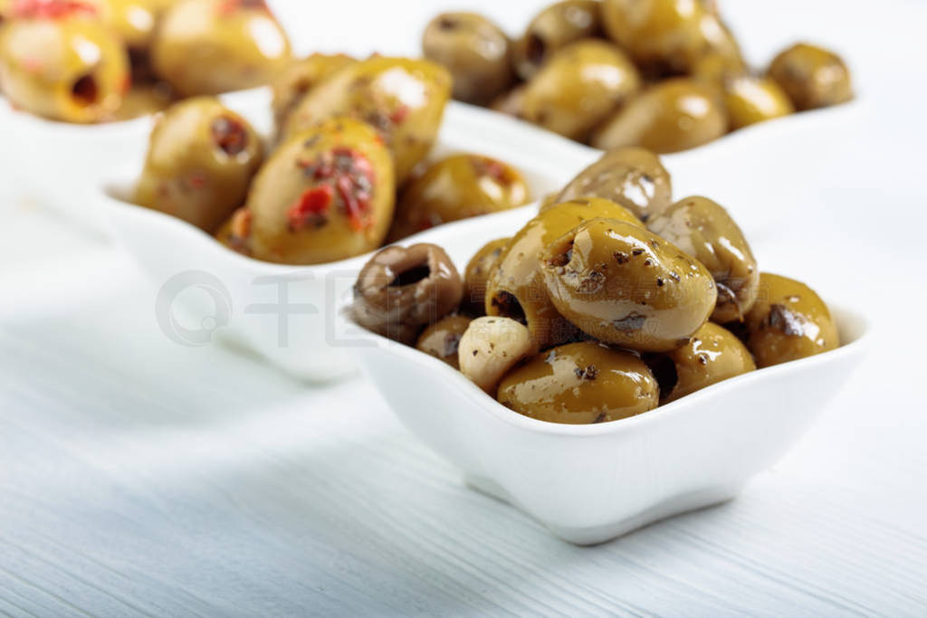 Spiced green olives in oil on a wooden table.