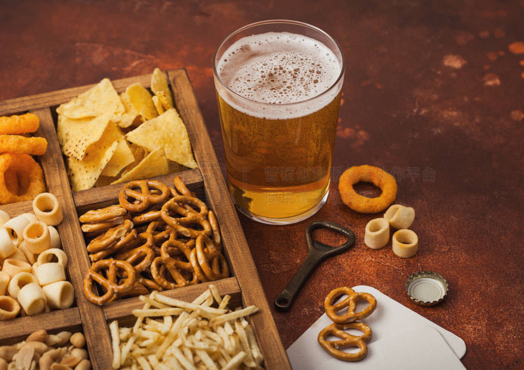 Glass of craft lager beer and opener with box of snacks on brown
