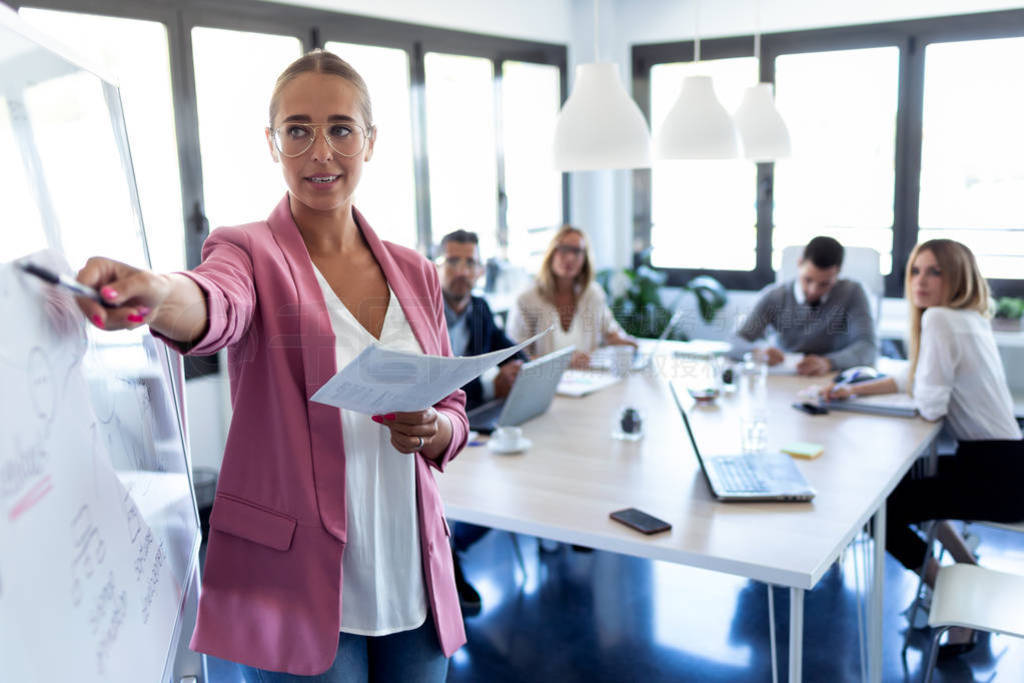 Elegant young businesswoman pointing at white blackboard and exp