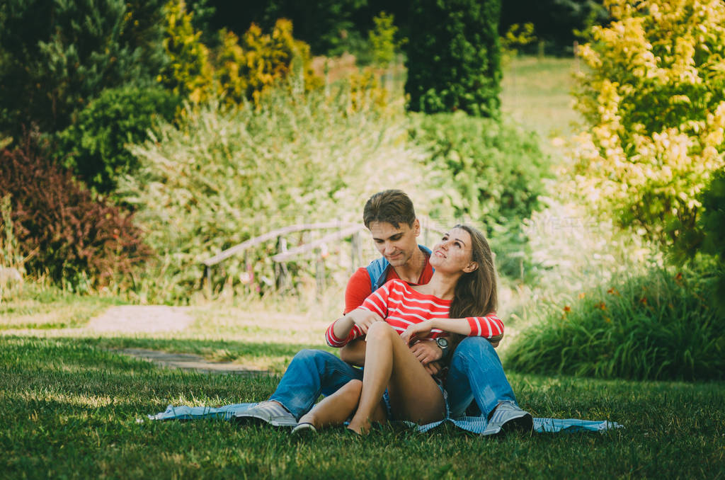 young loving couple is sitting on a plaid in the park, hugging,